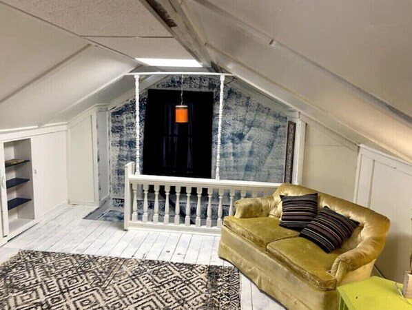 Relax in this charming attic room with a cozy sofa, patterned rug, and shelving units.