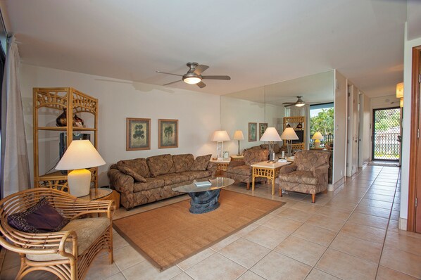 A spacious living room with a large sofa, two armchairs, a coffee table, and a ceiling fan.