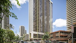 A tall hotel with multiple floors, a checkered facade, and a corner parking sign. - Aston Waikiki Sunset 1BMV | Mountain Views – Heated Pool & Spa (Honolulu)