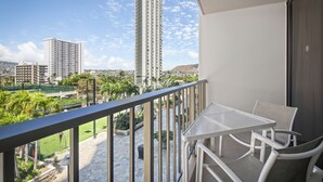 Un balcón con mesa y sillas, con vistas a un área ajardinada con palmeras y una vista distante de edificios altos.