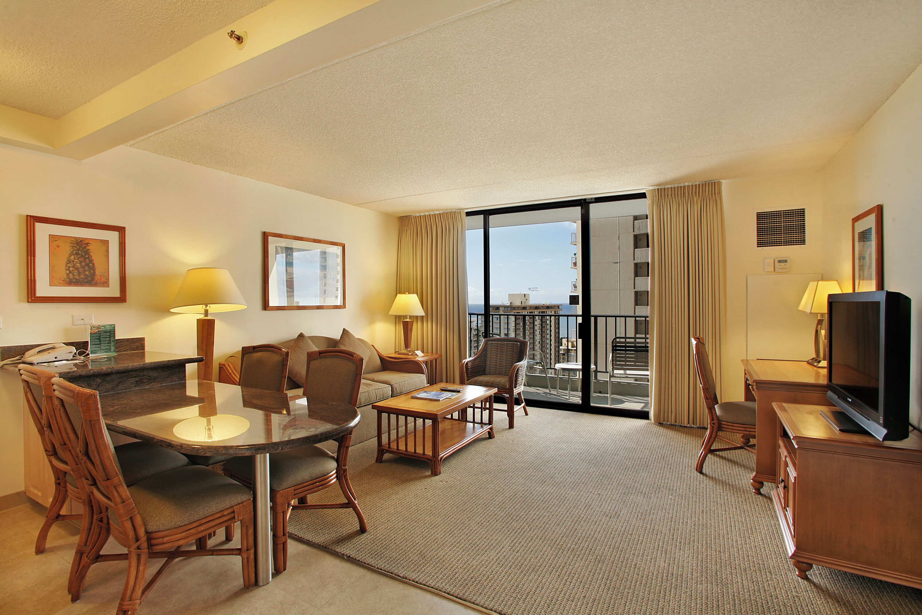 A hotel room with a dining area, a sofa, a TV, and a balcony with a view.