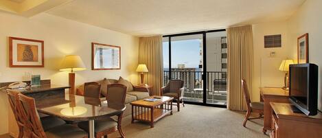 A hotel room with a dining area, a sofa, a TV, and a balcony with a view.