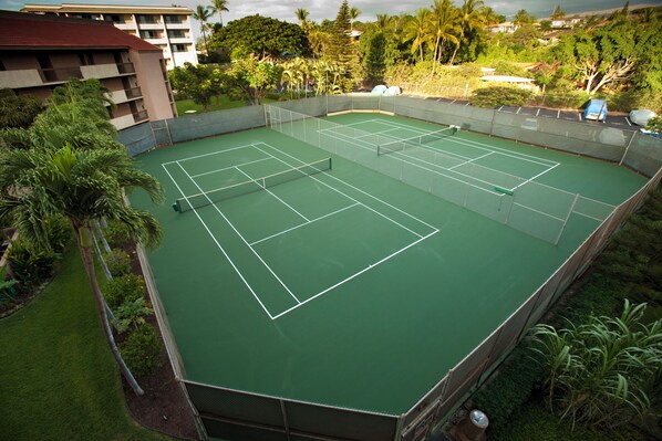 En tenniskort omgiven av grönska och en byggnad.