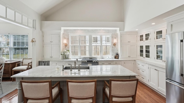 A spacious kitchen with a large island, white cabinetry, and a stainless steel refrigerator.