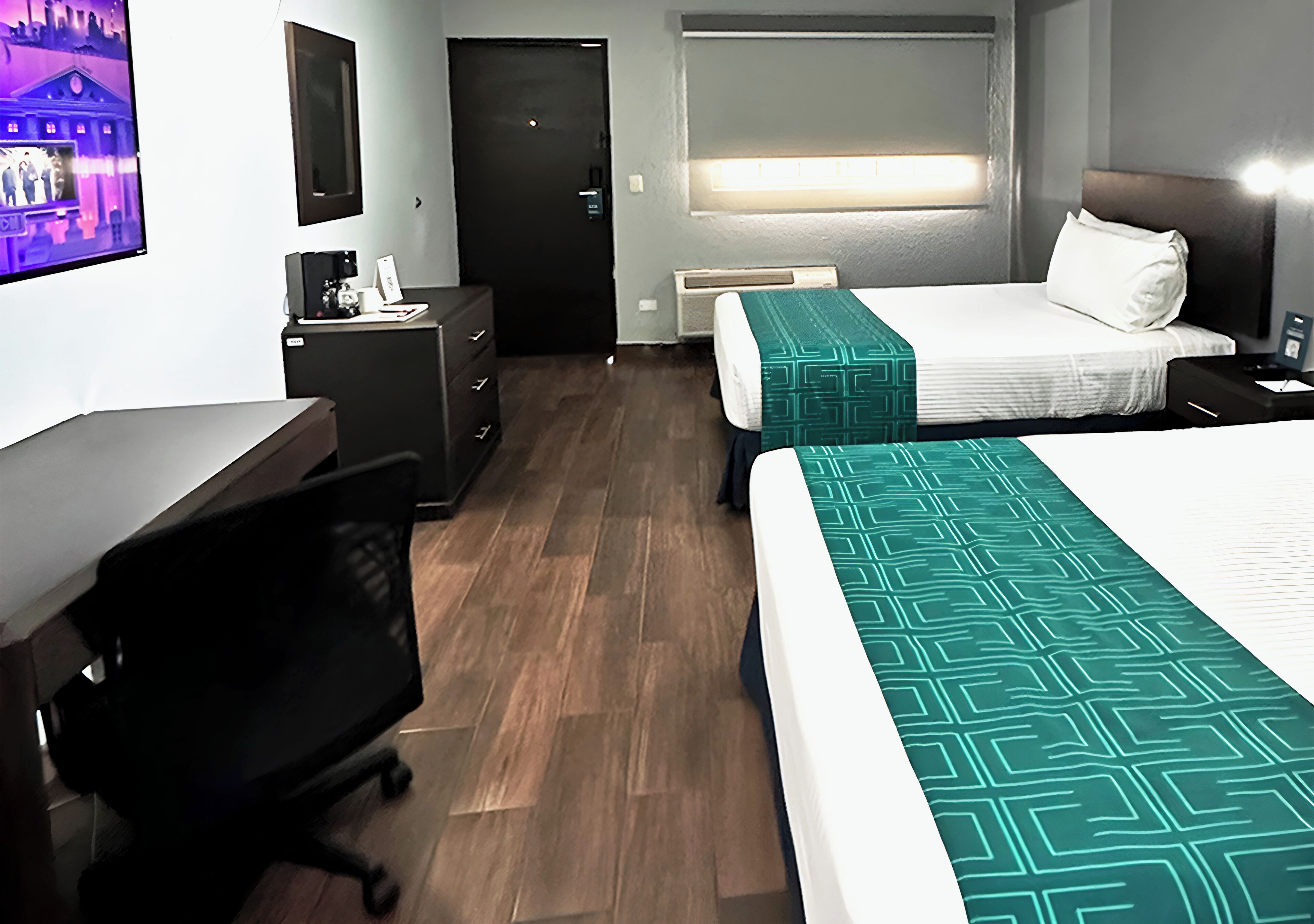 Une chambre d’hôtel avec deux lits, un bureau, une chaise, une télévision et une fenêtre avec des stores.
