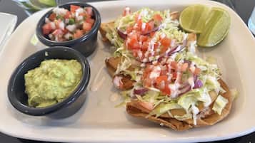 Un plato con dos porciones de guacamole y una bandeja de nachos cubiertos de lechuga, tomates y cebolla.
