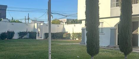 Une zone herbeuse bien entretenue, avec un lampadaire et deux arbres hauts et élancés.