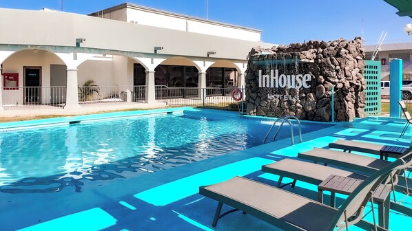 A swimming pool with lounge chairs and a rock wall with the InHouse Hotels logo.