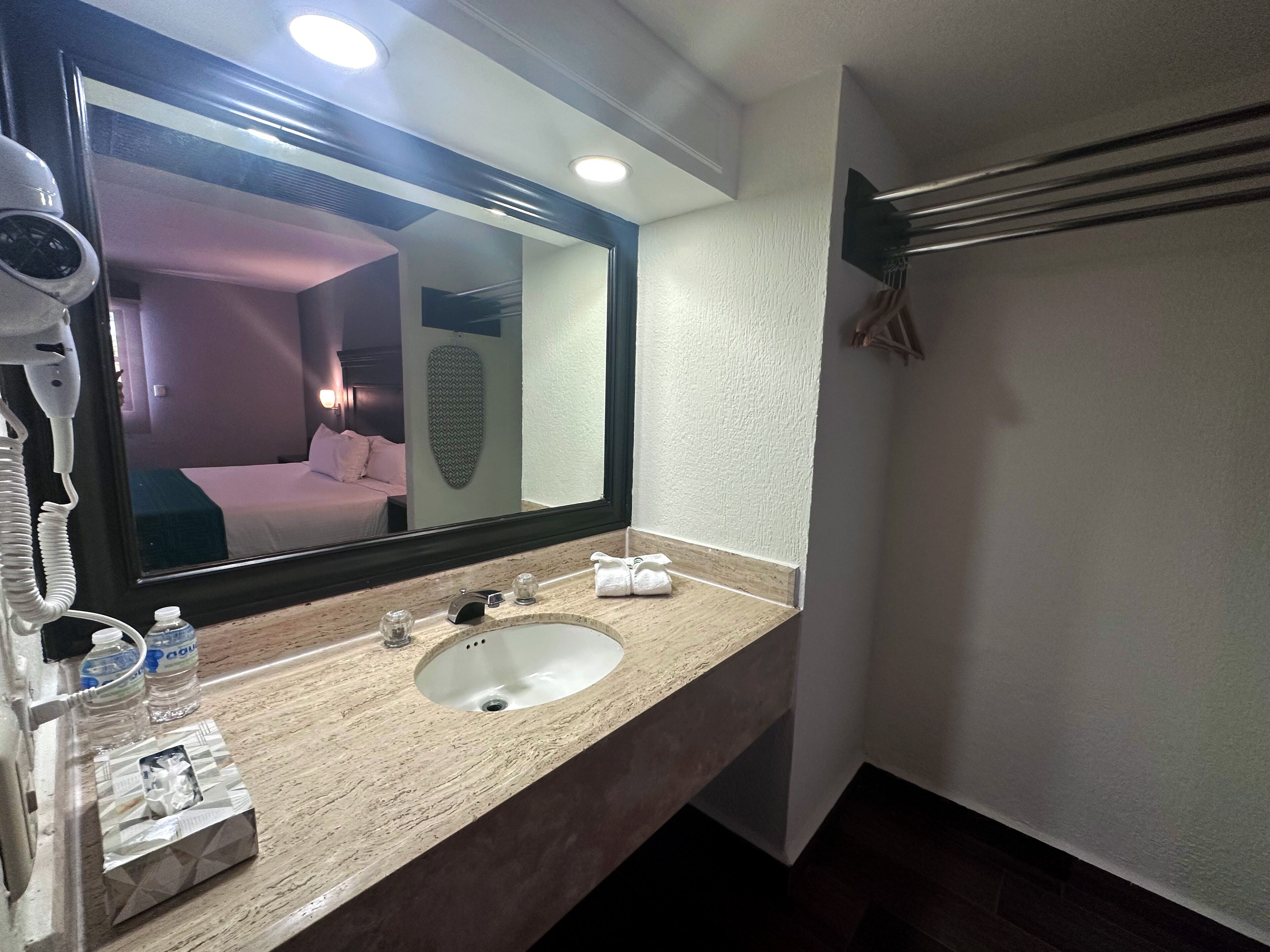 Baño de hotel con un espejo grande, un lavabo, un secador de pelo y un perchero para toallas.