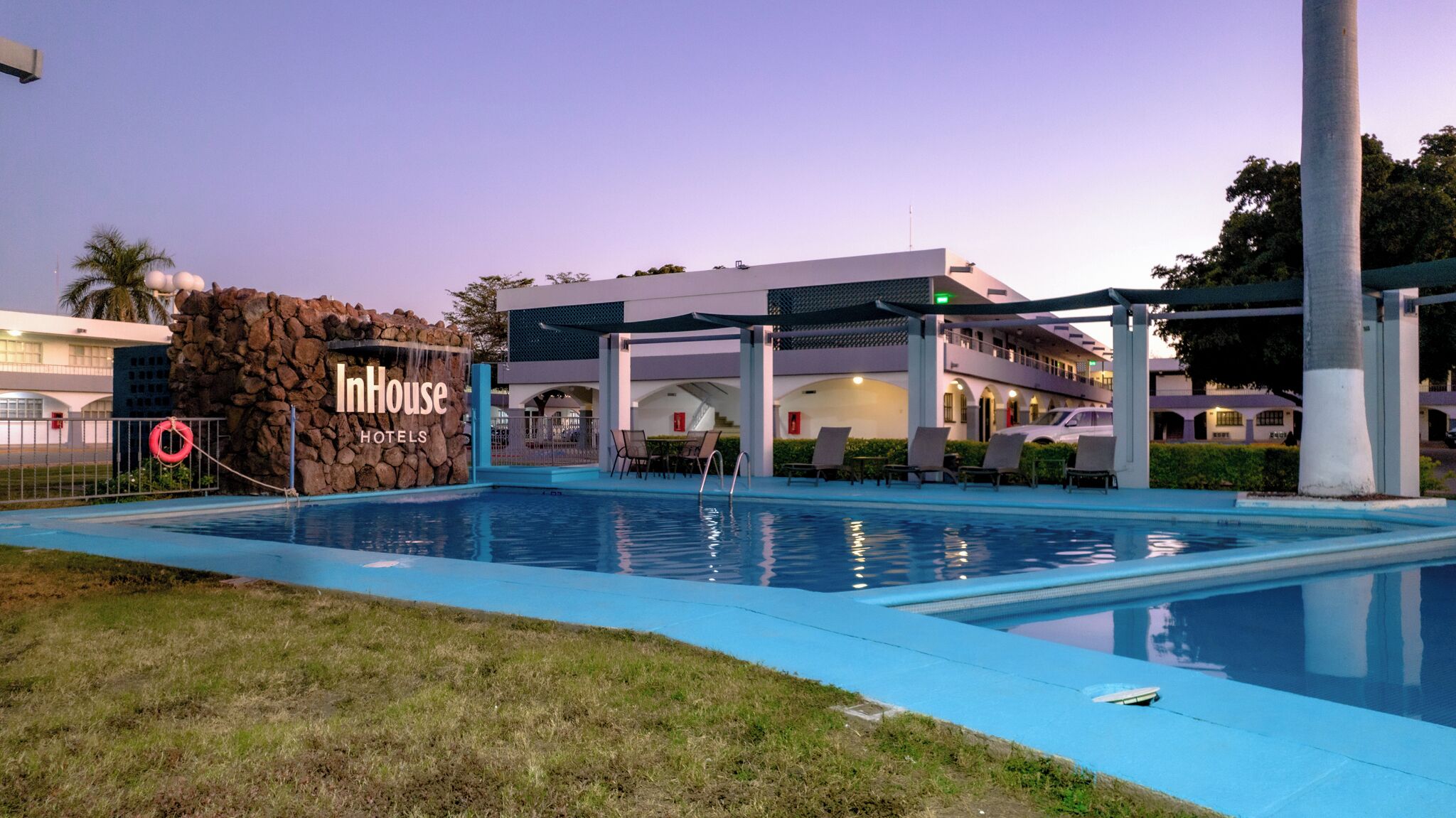 Zona de piscina de un hotel con pared de piedra, sillas de descanso y un cartel que dice "InHouse Hotels".