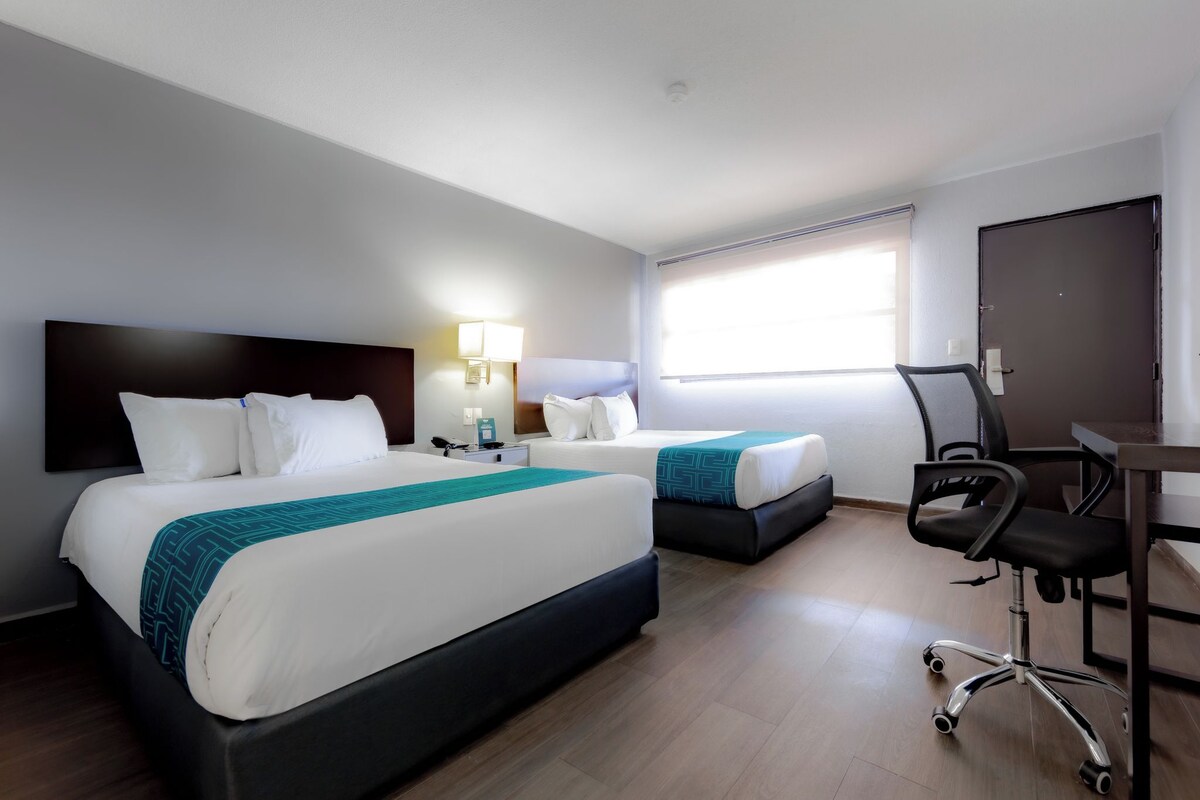 A hotel room with two beds, a desk, a chair, and a window.
