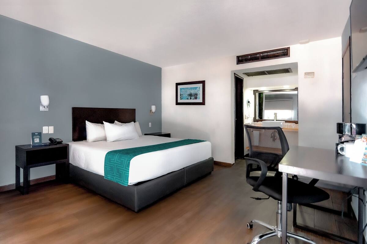 A hotel room with a bed, bedside table, desk, chair, and a mirror.
