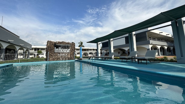 Une piscine d’hôtel avec un panneau indiquant « InHouse Hotels » et un ciel bleu clair.