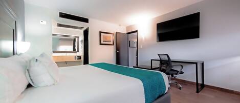A hotel room with a bed, desk, chair, TV, and a bathroom with a mirror and sink.