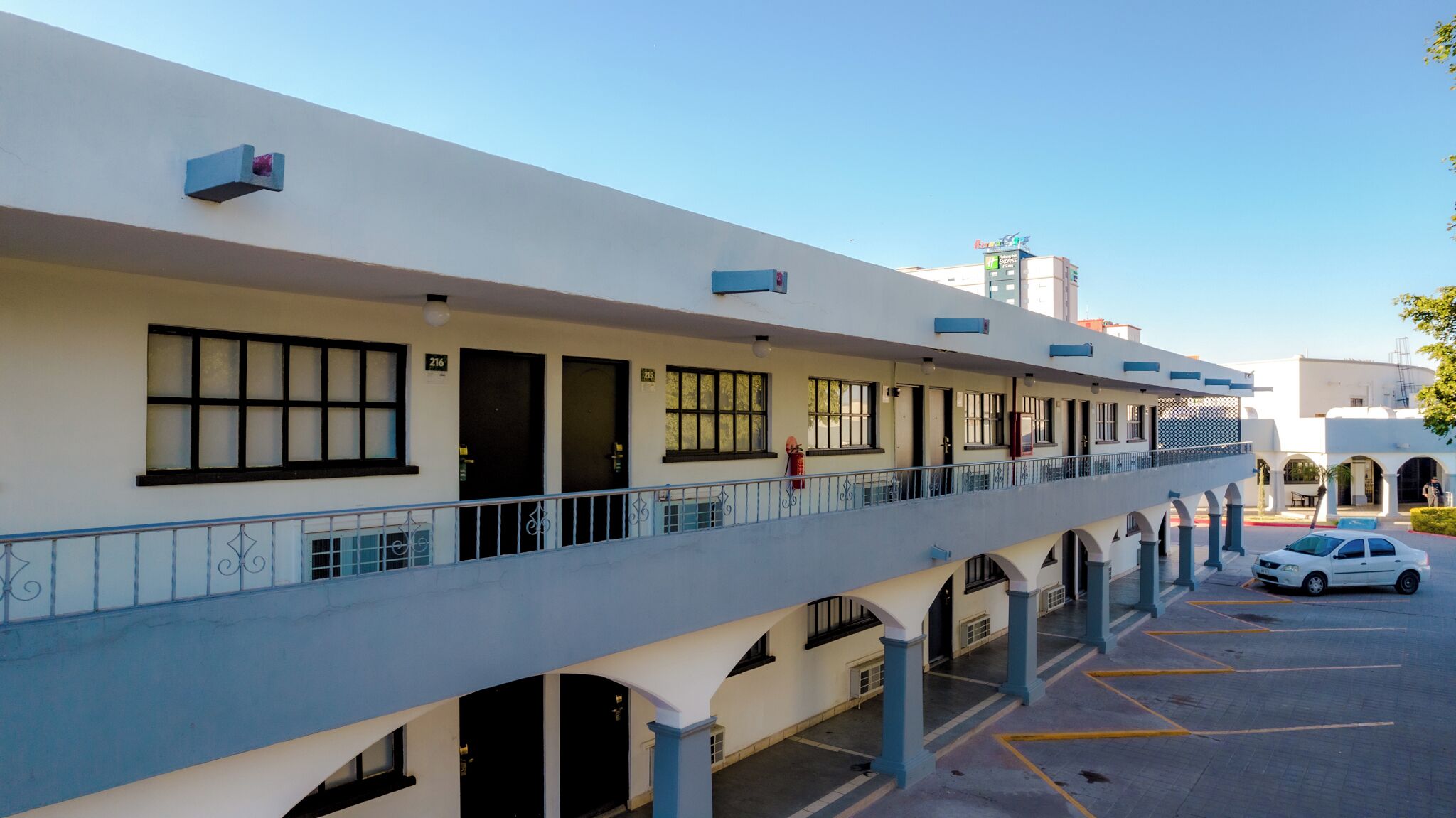 A multi-story hotel with a covered outdoor area, multiple balconies, and a parking lot.