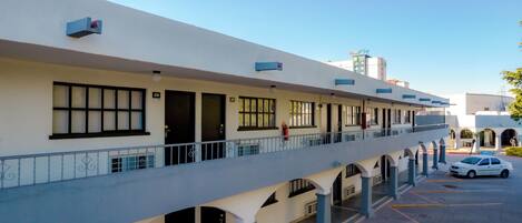 A multi-story hotel with a covered outdoor area, multiple balconies, and a parking lot.