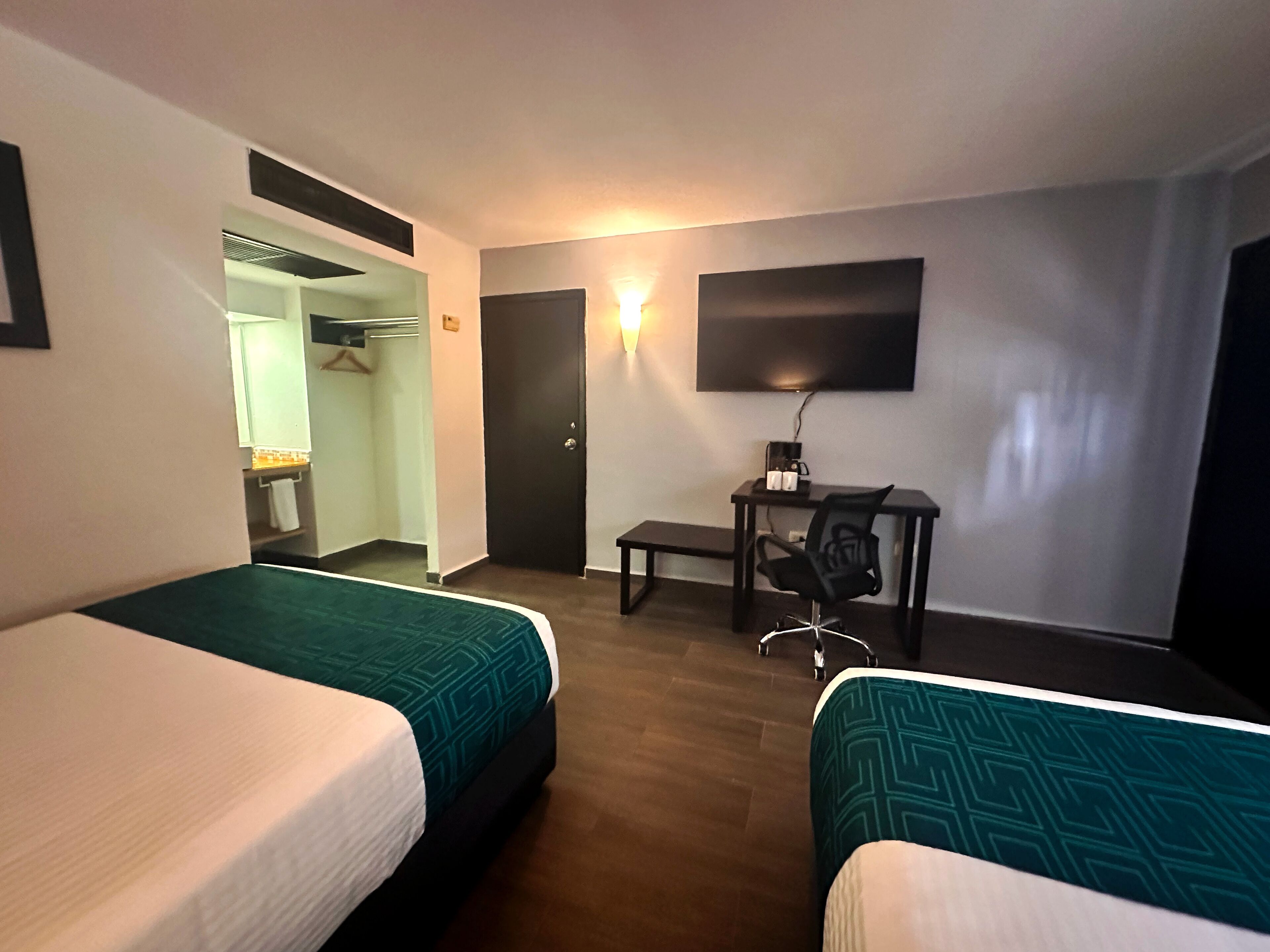 A hotel room with two beds, a desk with a chair, a TV, and a wardrobe.