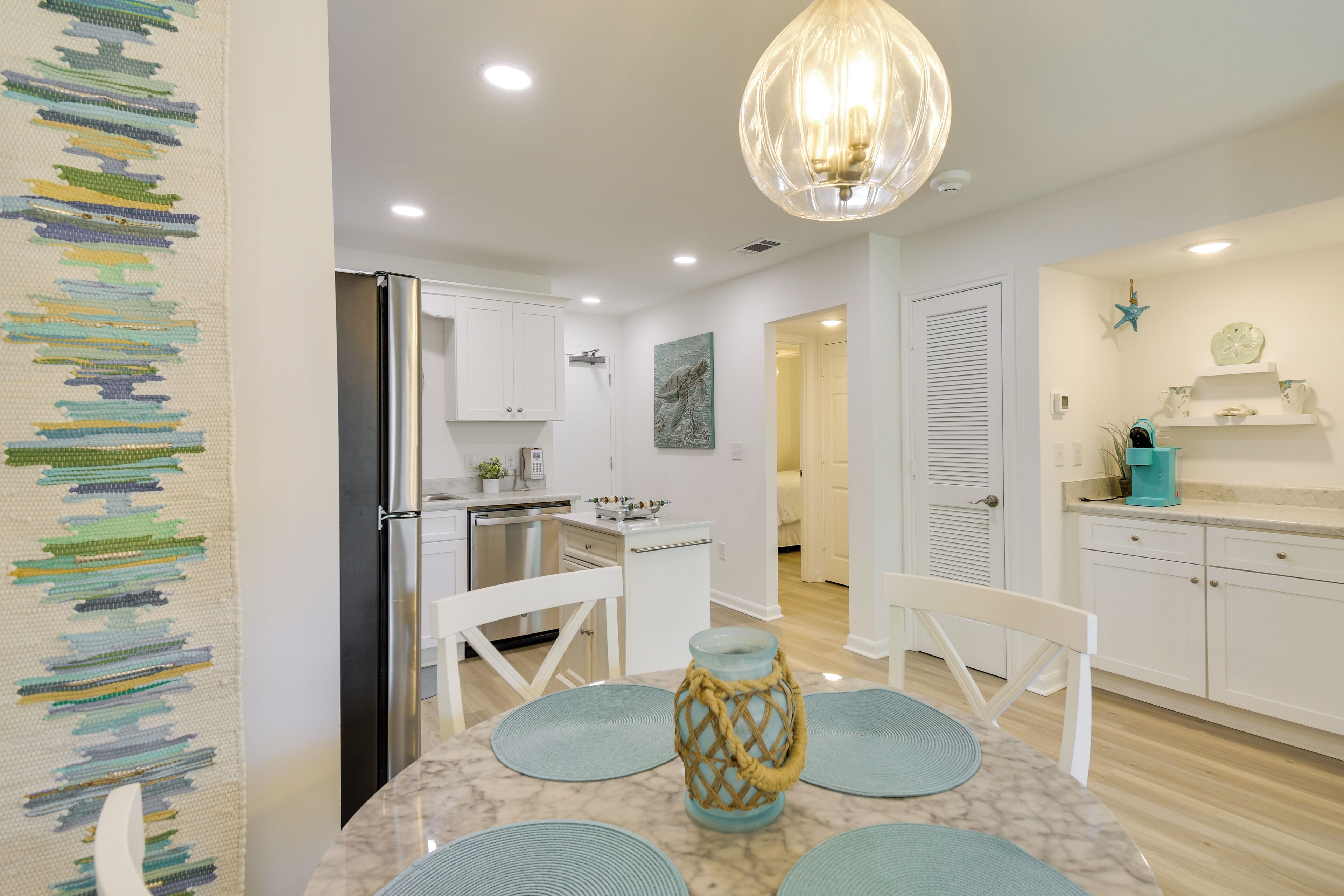 Una cocina moderna con armarios blancos, un refrigerador de acero inoxidable y un comedor con una mesa de mármol y caminos de mesa azules.
