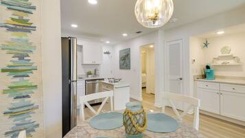 Una cocina moderna con armarios blancos, un refrigerador de acero inoxidable y un comedor con una mesa de mármol y caminos de mesa azules.