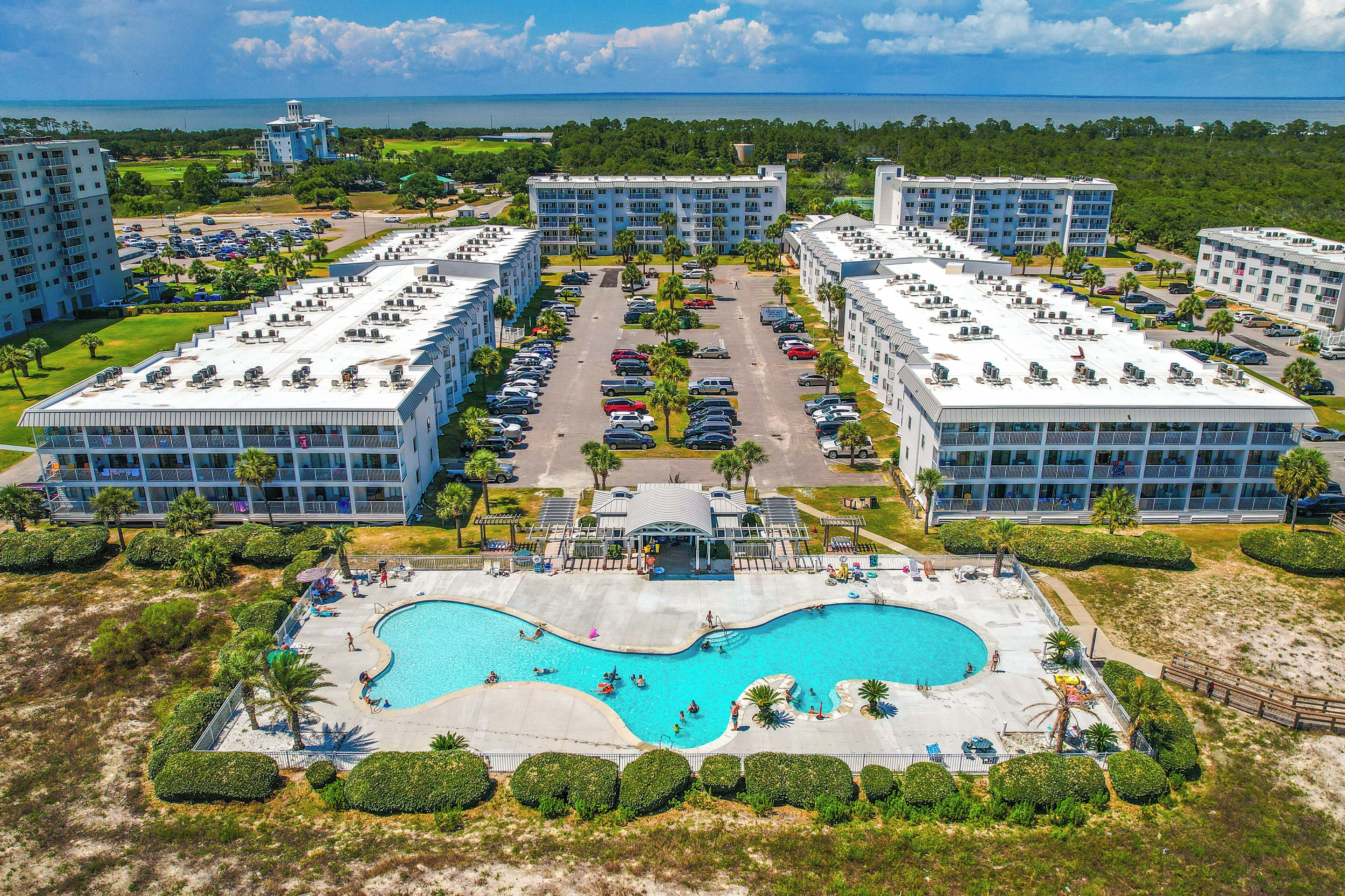 Un resort con varias construcciones, un área de piscina central y vista al océano.