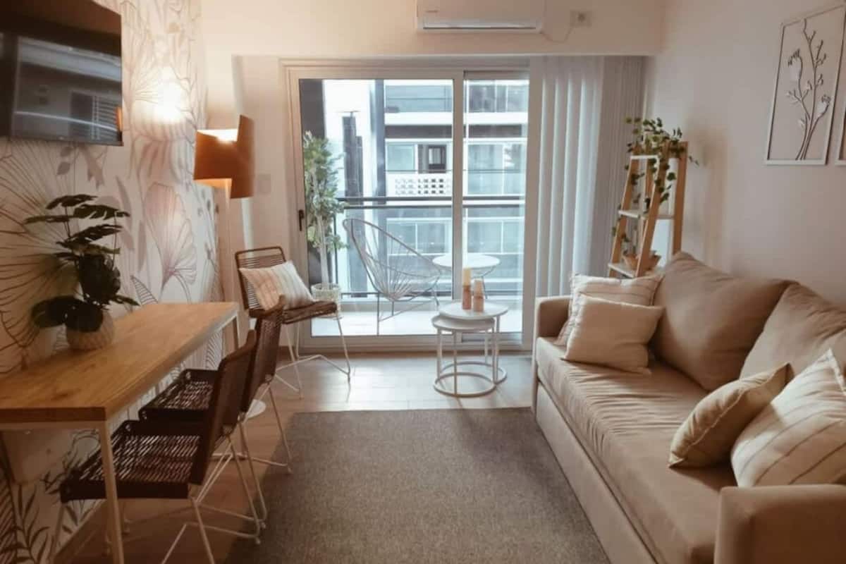 Un salon moderne comprenant un canapé, une table à manger avec des chaises, une petite table ronde et un balcon offrant une vue sur les immebles.