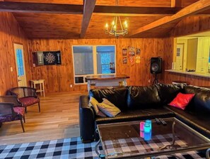 A cozy room with wooden walls, a black leather sofa, a checkered coffee table, and a chandelier.