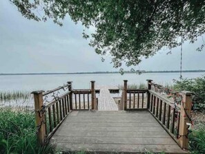 A wooden pier leading to a calm lake with a clear view of the distant shoreline.