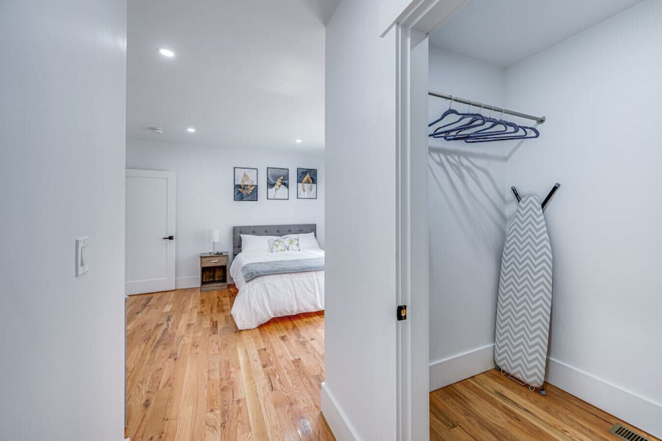 Une chambre à coucher comprenant un lit, une table de chevet, un étendoir fixé au mur et une porte donnant sur une autre pièce.