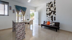 Amplia sala de estar con una encimera de cocina, una mesa de comedor con sillas, un sofá con cojines y un panel decorativo en la pared.