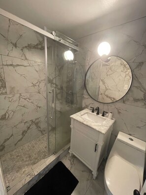 Un baño con ducha de vidrio, un lavamanos con espejo y un inodoro.