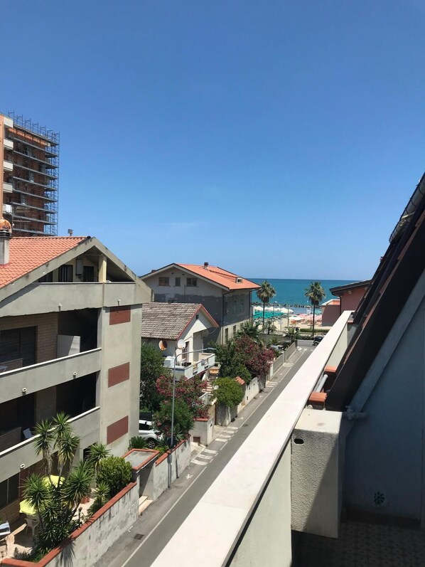 Une rue résidentielle bordée de maisons, un ciel bleu azur et la mer en arrière-plan.