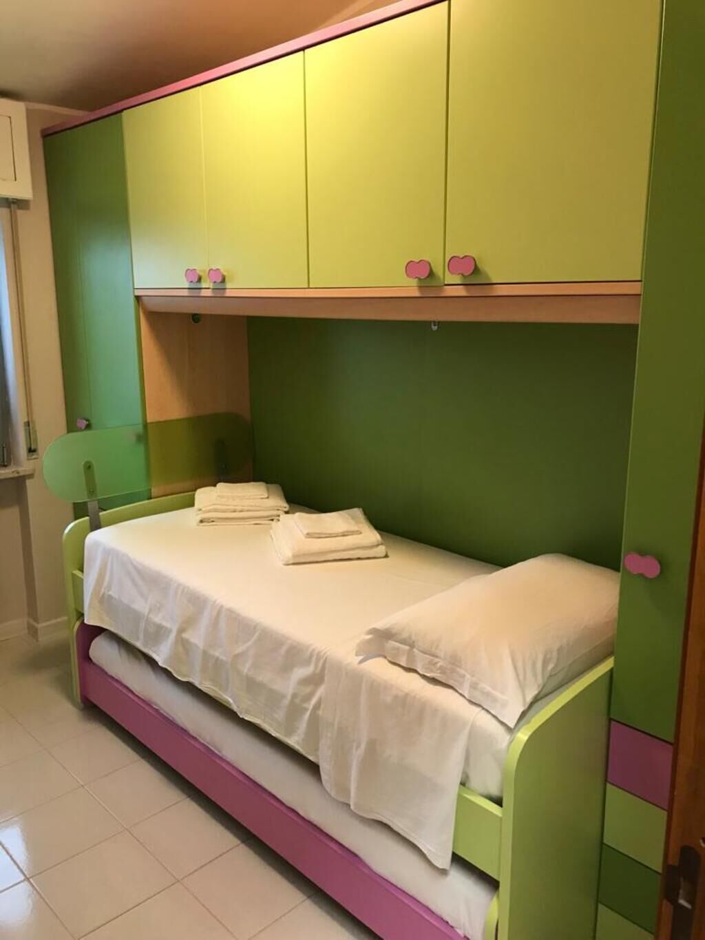 Een eenpersoonskamer met groene en roze wanden, een wit sprei en een groen hoofdeinde.