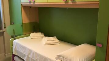 Een eenpersoonskamer met groene en roze wanden, een wit sprei en een groen hoofdeinde.