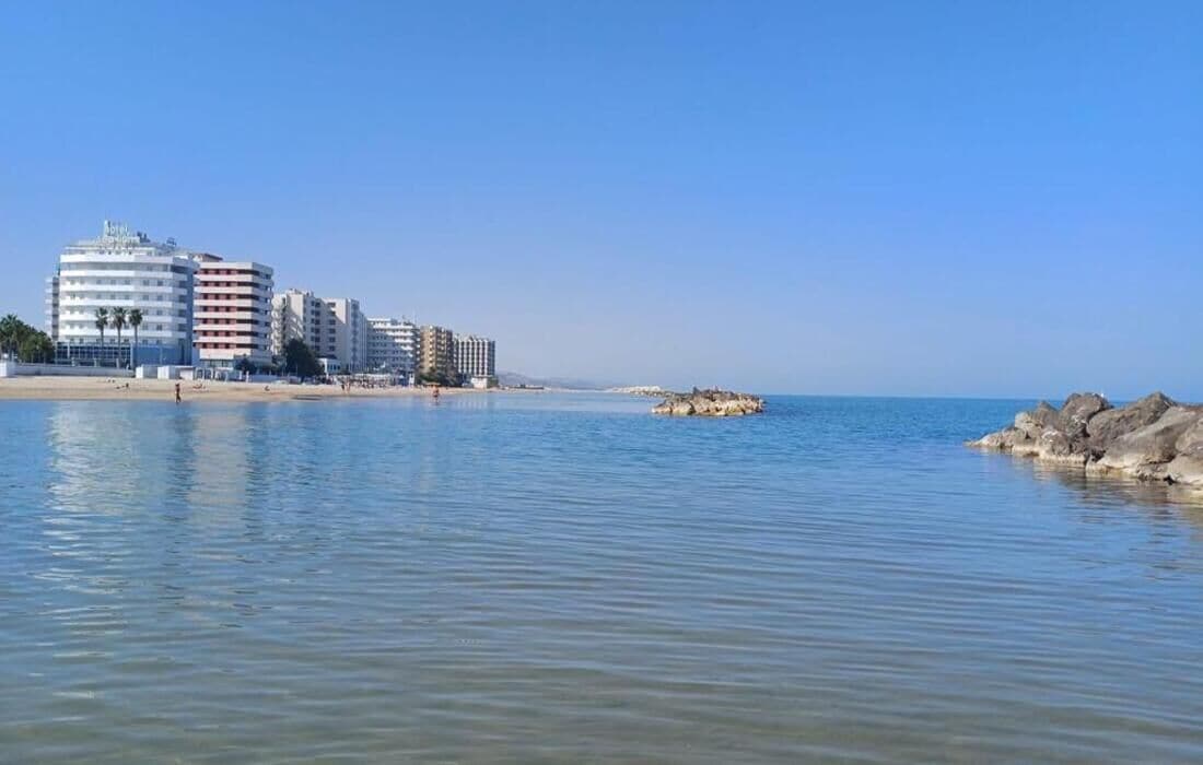 Un hotel sulla costa con diversi edifici, una spiaggia e acque calme.
