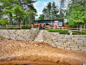 Situated in a wooded area, this cabin features a front porch with outdoor seating and a door.