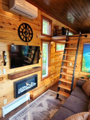 Cozy cabin interior with a large flat-screen TV, fireplace, and comfortable seating area.