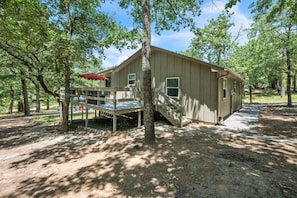 A single-story wooden cabin with a covered deck and a staircase leading to a porch.