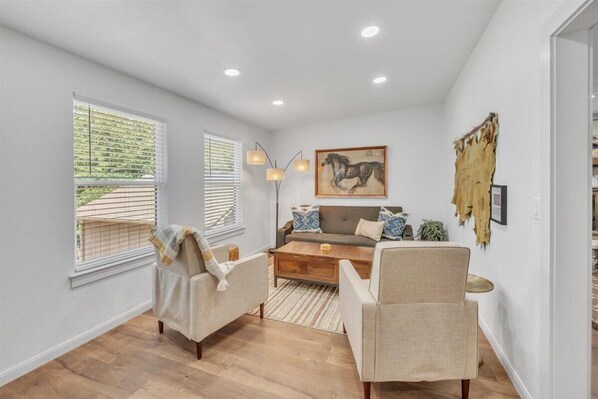 A modern living room with a sofa, two armchairs, a coffee table, and a floor lamp. There is a painting on the wall and a piece of indigenous art.