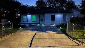 A residential house with a paved driveway, chain-link fences, and a well-lit entrance. - Comfy casa Duplex by Southside Lions (San Antonio)