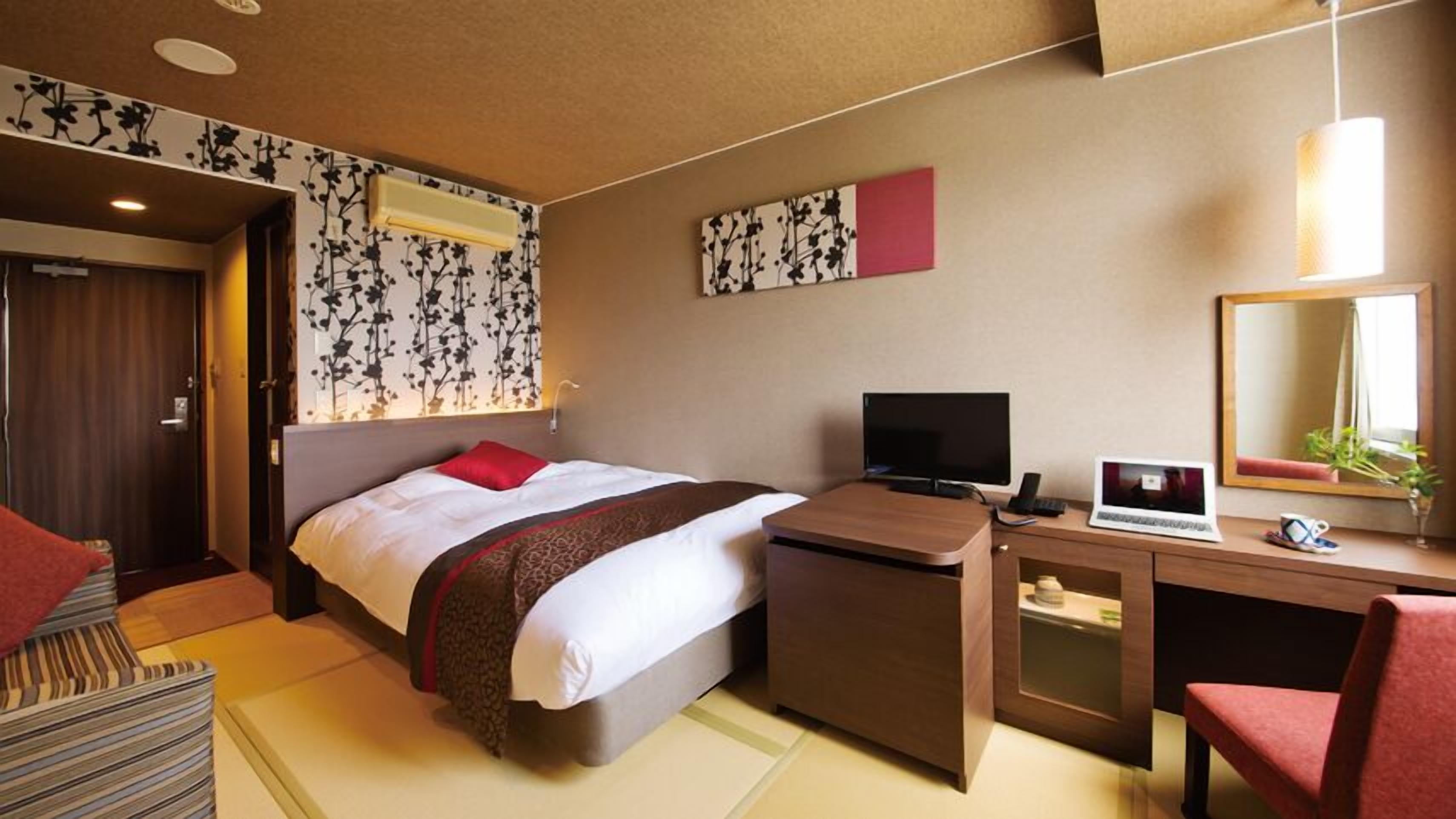 Habitación de hotel con cama, escritorio, silla, televisor y espejo.