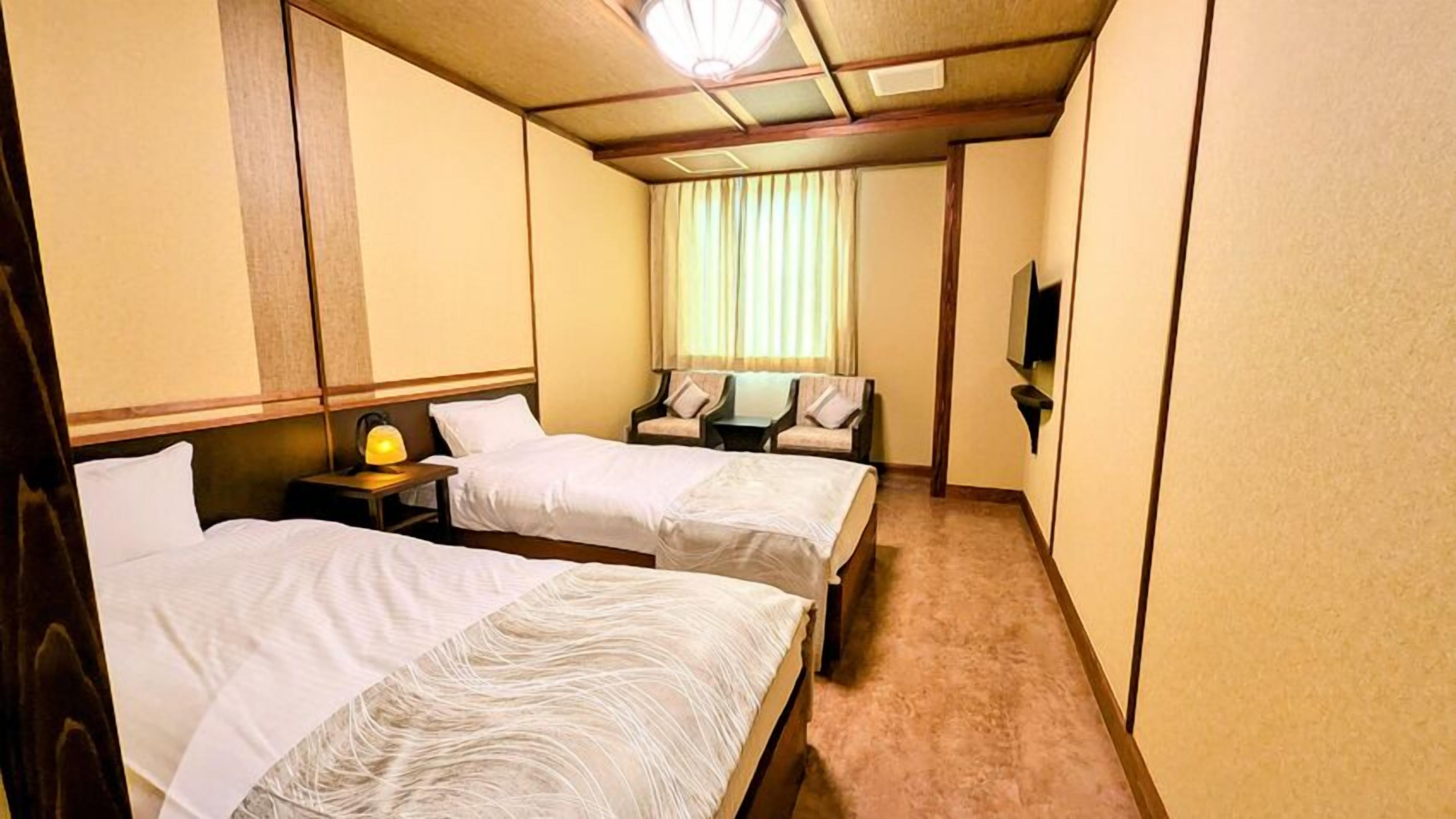 A hotel room with two beds, a nightstand with a lamp, a television, and a window with curtains.