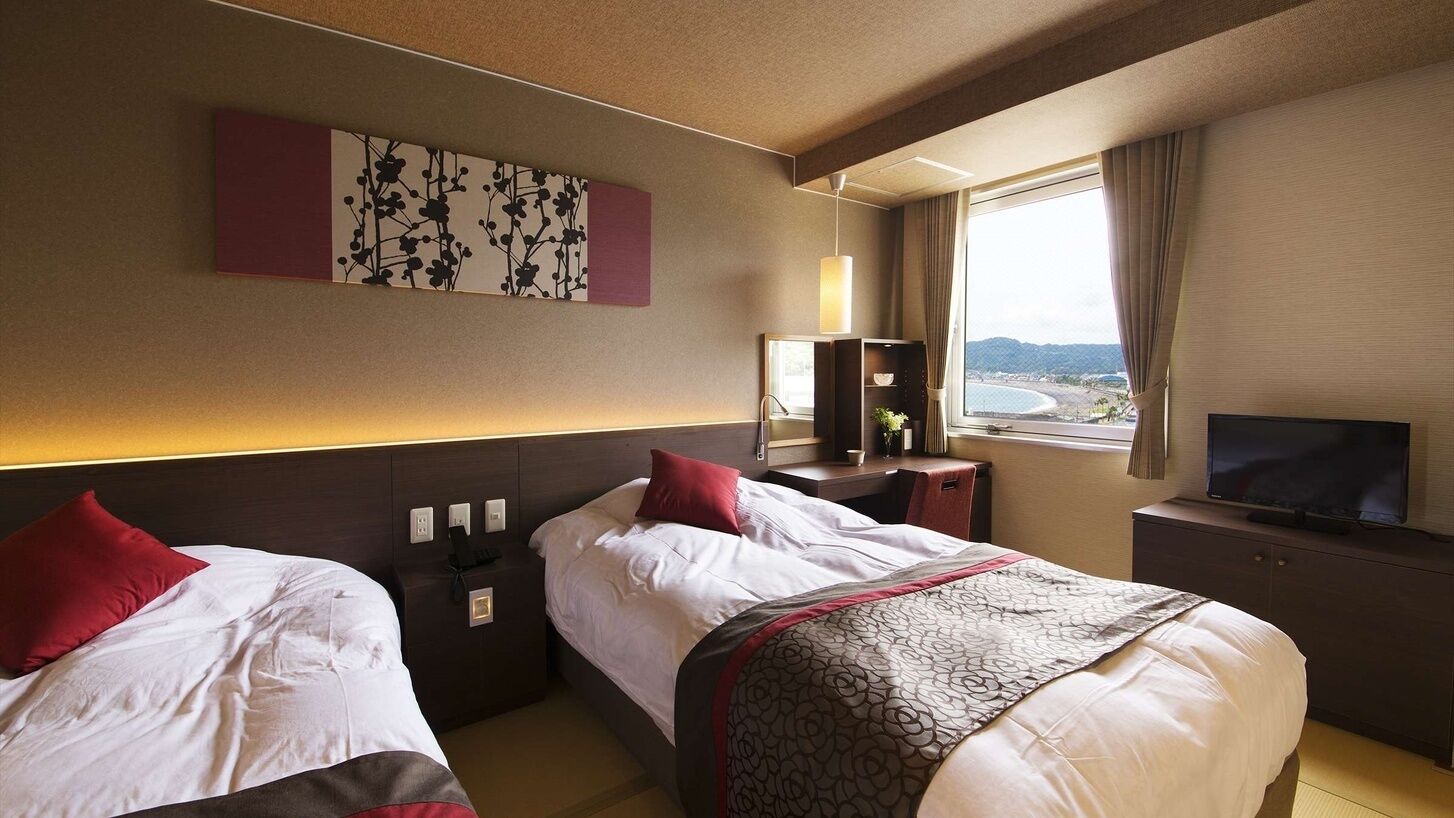 A hotel room with two beds, a TV, a window with a view, and a painting on the wall.