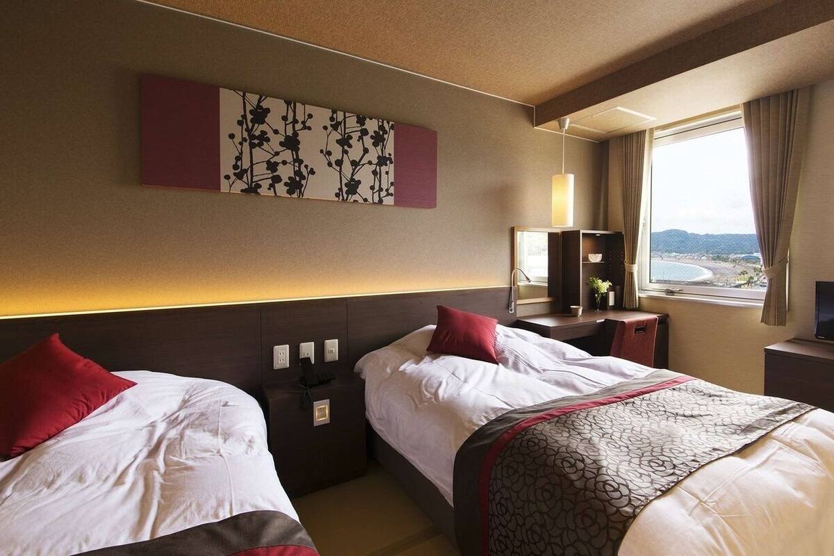 A hotel room with two beds, a TV, a window with a view, and a painting on the wall.