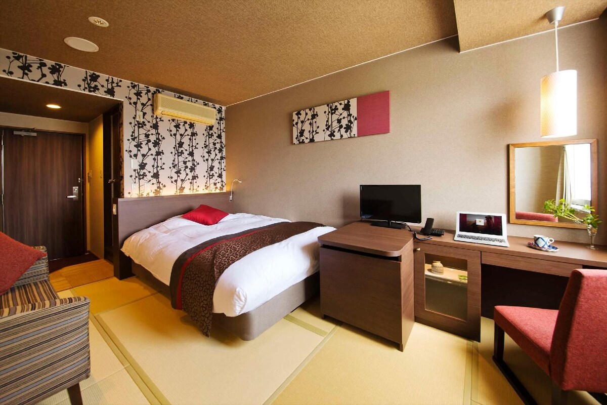 A hotel room with a bed, desk, chair, and a mirror.