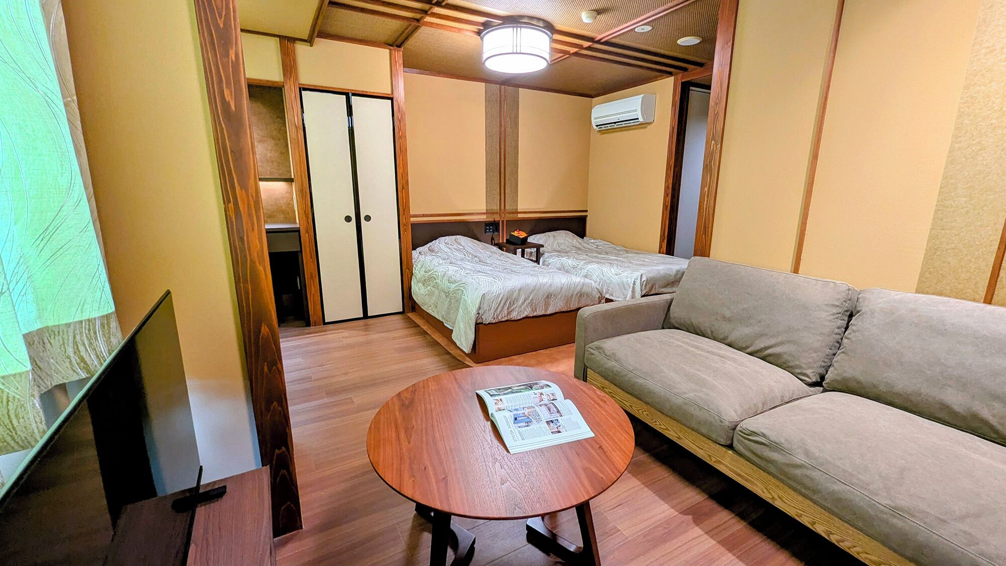 Una habitación compacta con sofá, cama con dos almohadas, una mesita con una revista y televisor.