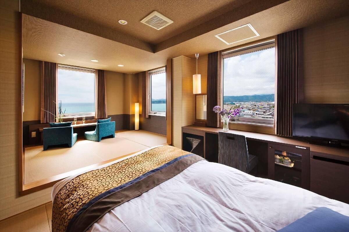 Een hotelkamer met een groot bed, zithoek, televisie en uitzicht op zee.