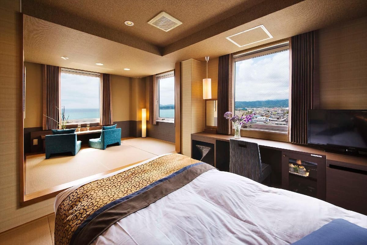 A hotel room with a large bed, seating area, TV, and a view of the sea.