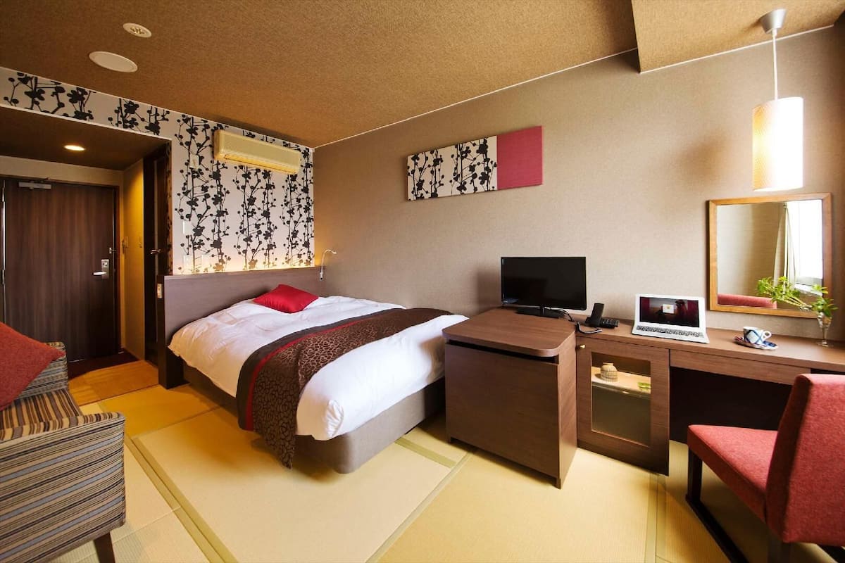 A hotel room with a bed, desk, chair, and a mirror.