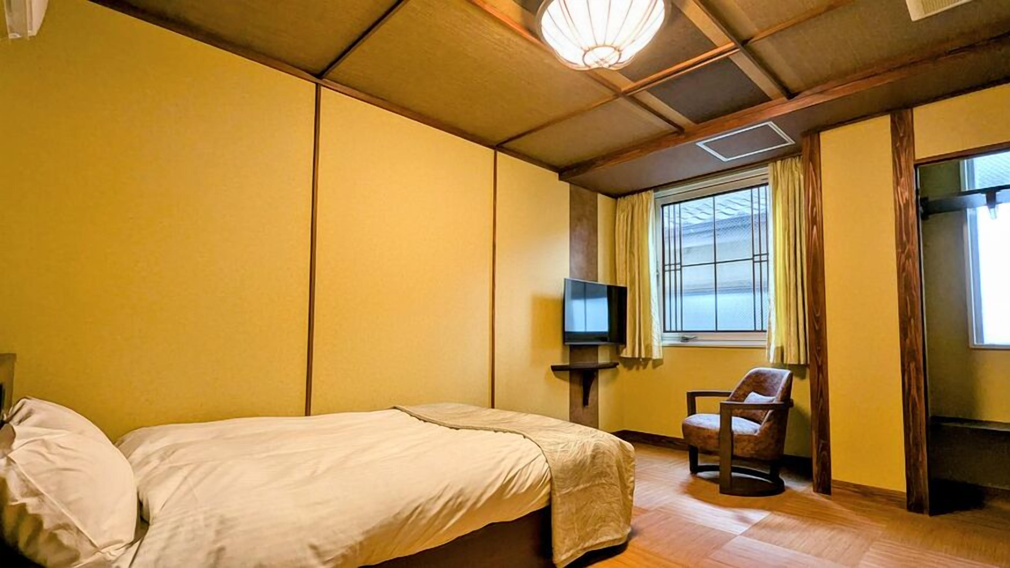 A hotel room with a bed, a chair, a television, and a window with curtains.