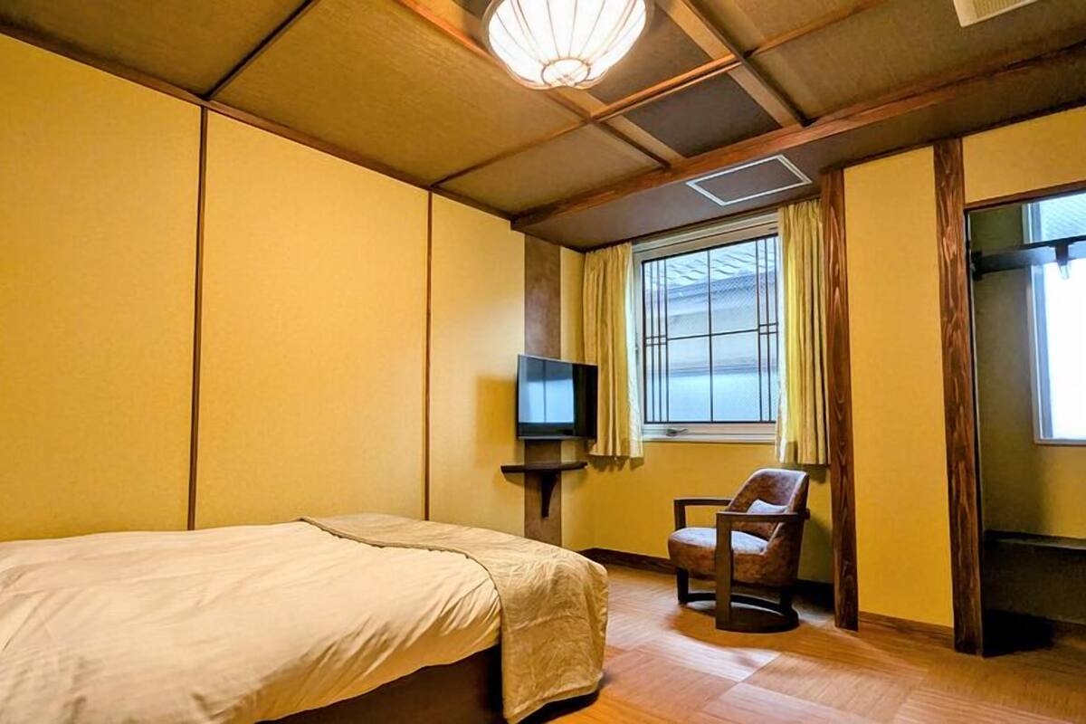 Een hotelkamer met een bed, een stoel, een televisie en een raam met gordijnen.